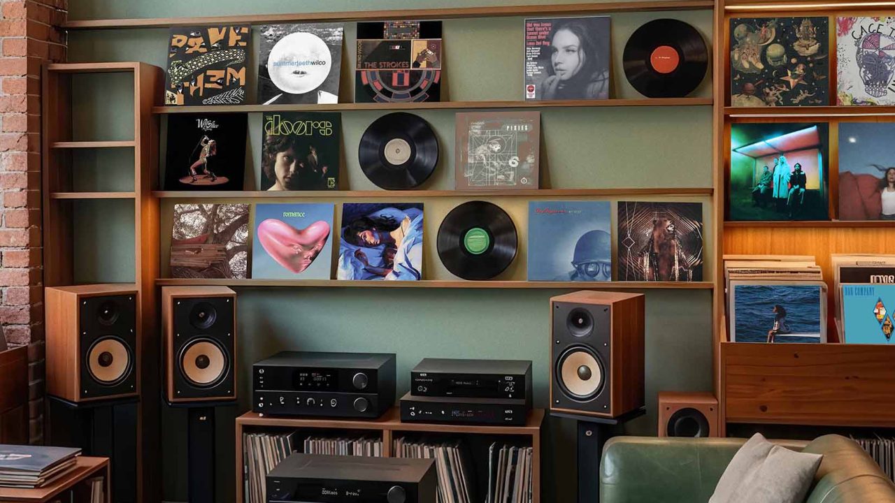 A cozy music room with a neon PLAYBACK ROOM sign, shelves of vinyl records, speakers, a turntable, and a green leather sofa.