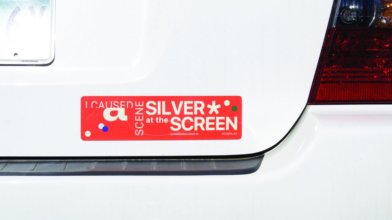 A red bumper sticker on a white car reads I caused a scene at the Silver Screen in white text, with colorful dots around the edges.