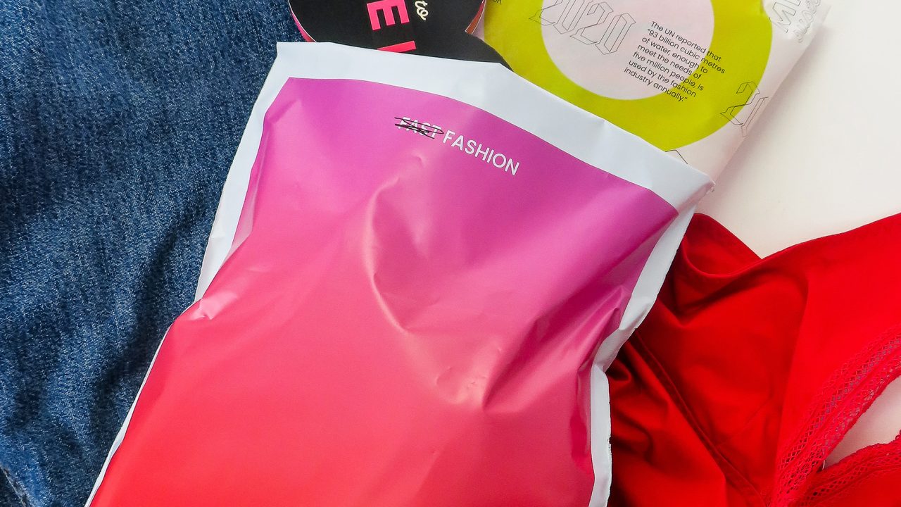 A pink and red package labeled THE LOOP on top of blue denim jeans, with a red garment and another circular package nearby.