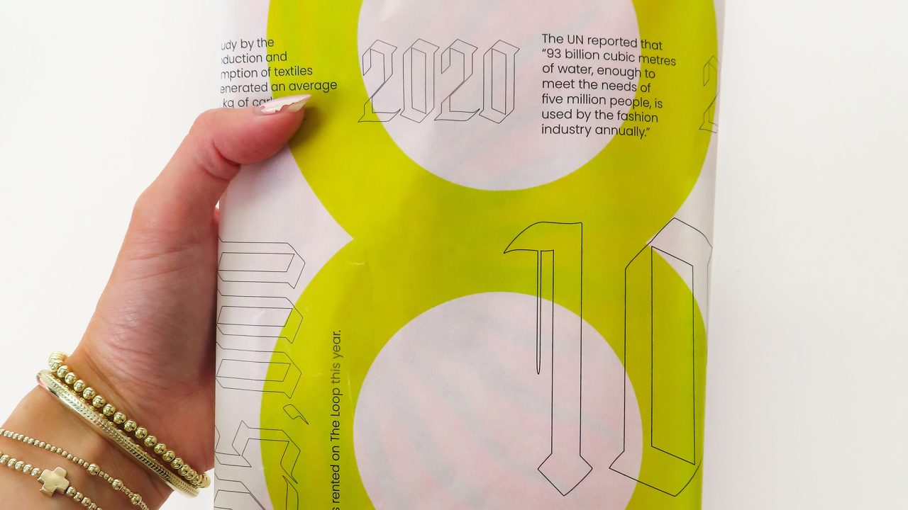A hand holding a white package with green circles, text, and numbers; some bracelets are visible on the wrist.