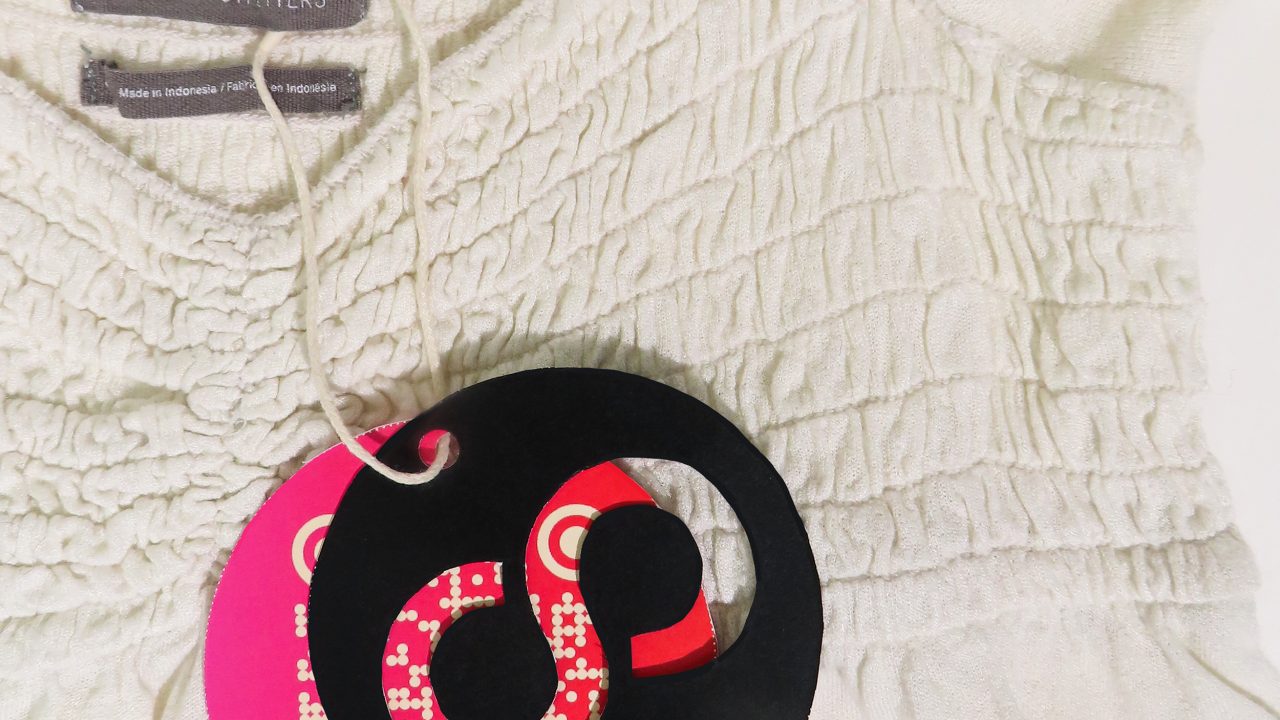 A white shirred Urban Outfitters top with attached circular black and pink tags, displayed clearly against a plain background.