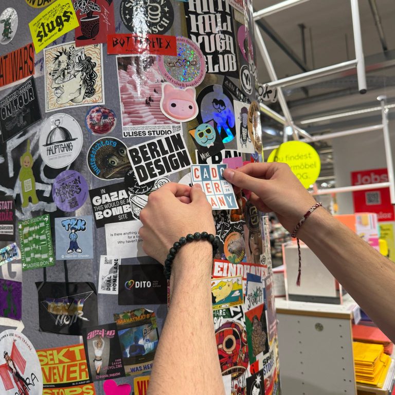 Two hands are placing a sticker that says CARD READER on a pole covered with various colorful stickers inside a store.