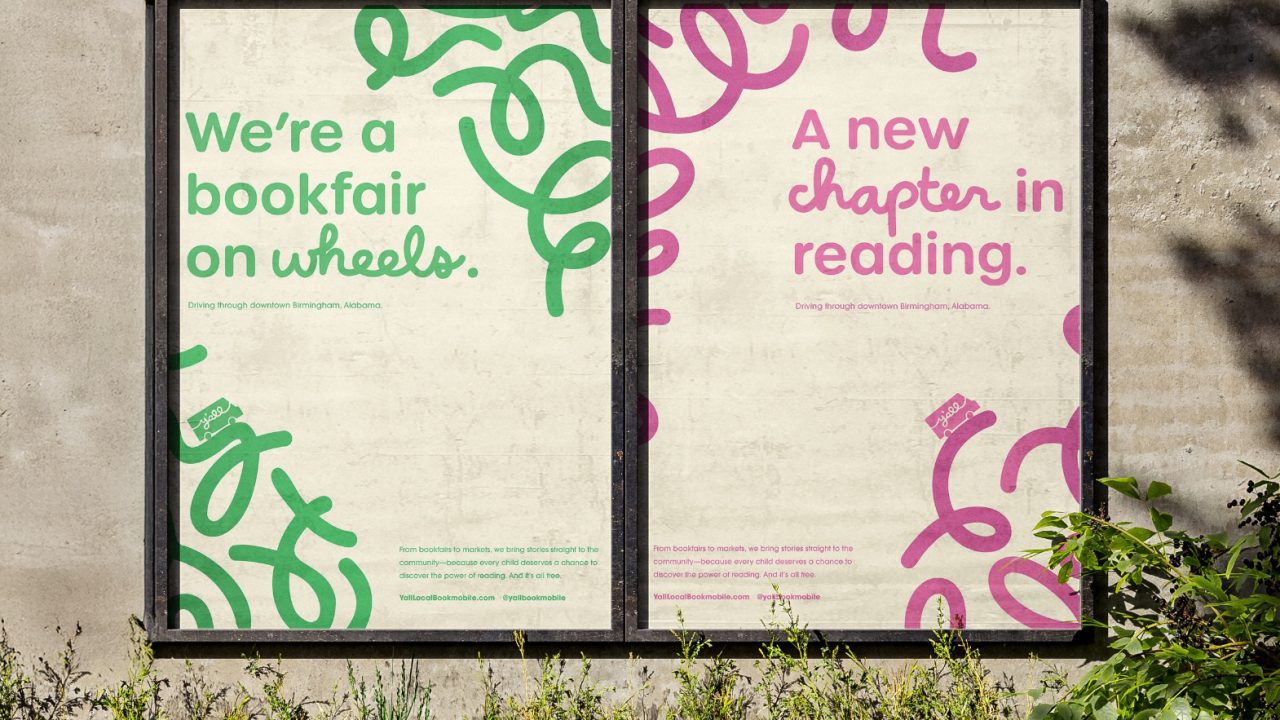 Two posters on a concrete wall read Were a bookfair on wheels. and A new chapter in reading. with green and pink swirly designs and plants in front.