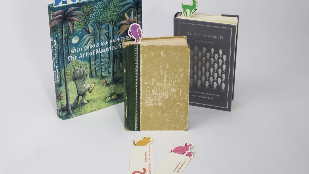 Three books are standing upright with animal-shaped bookmarks sticking out, and three more bookmarks lie flat in front on a white background.