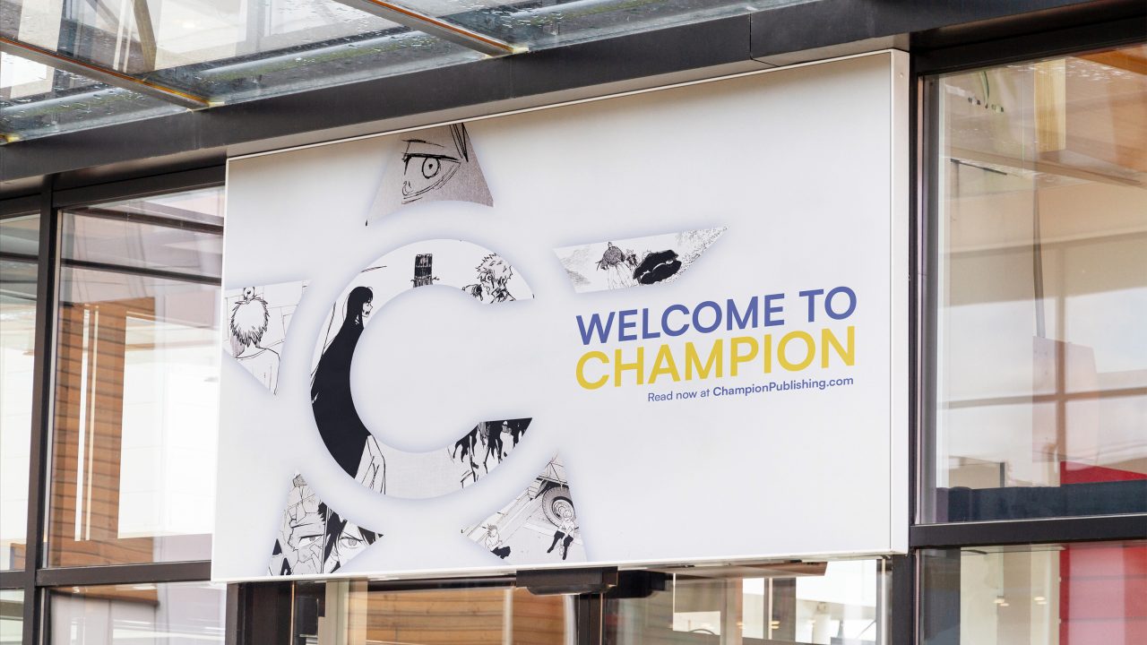 Large sign with a stylized C and star design, featuring the text Welcome to Champion and a website link, displayed on a modern building exterior.