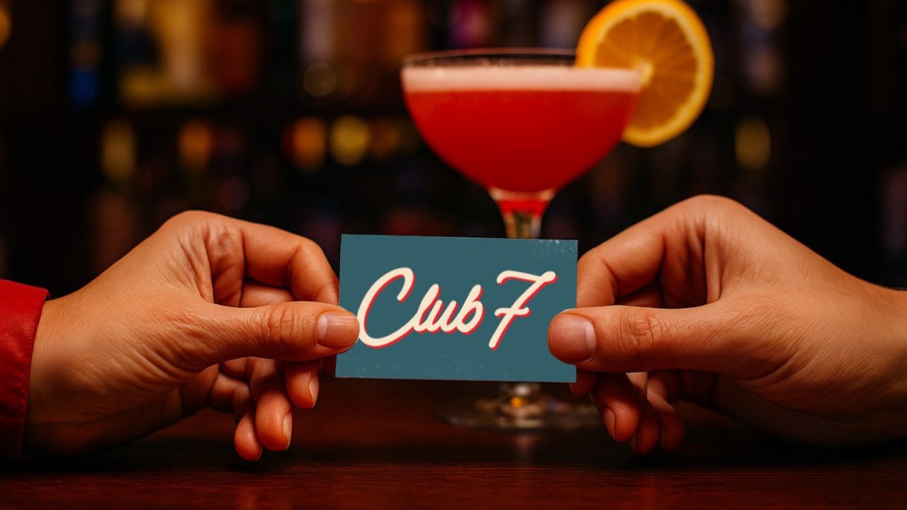 Two hands hold a card that reads Club 7 in front of a pink cocktail garnished with a lemon slice, with a blurred bar background.