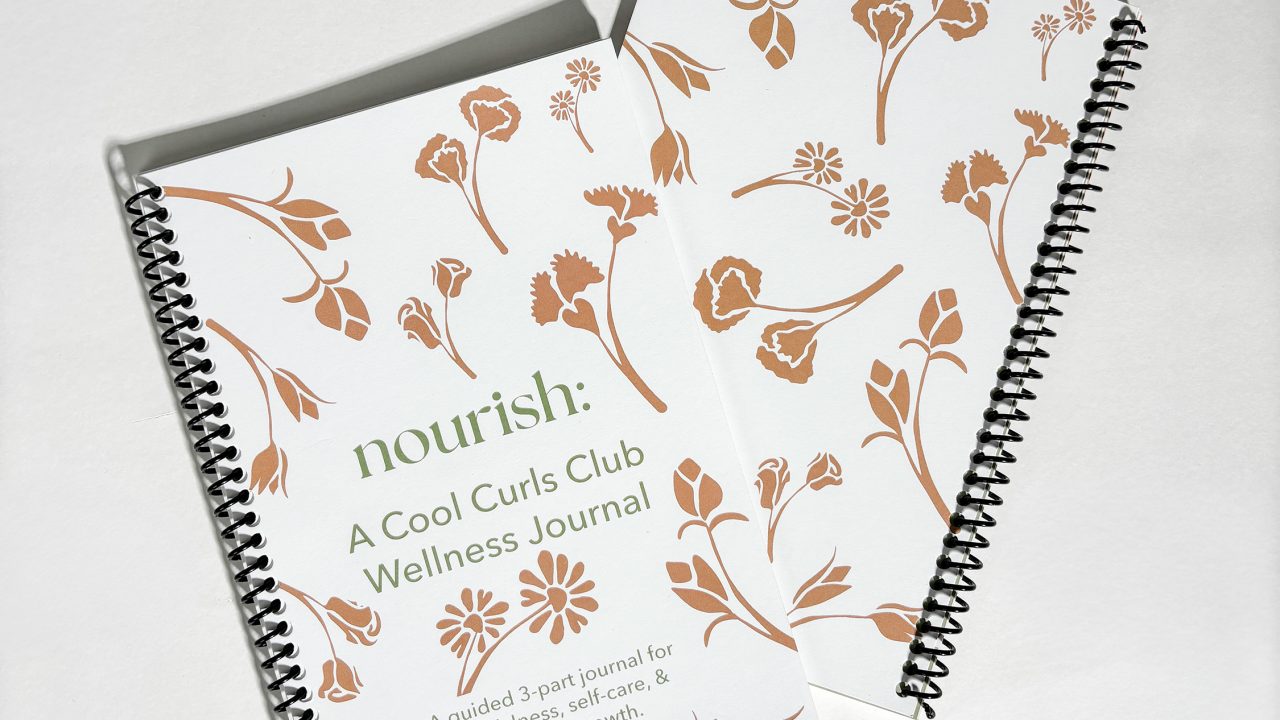 Two spiral-bound wellness journals with brown floral designs on white covers; one journal shows the title nourish: A Cool Curls Club Wellness Journal.