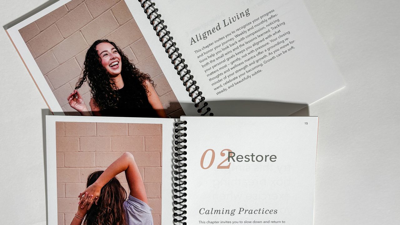 Two open spiral-bound booklets display pages titled Grow with a woman smiling and Restore with a woman stretching, both against a plain wall.