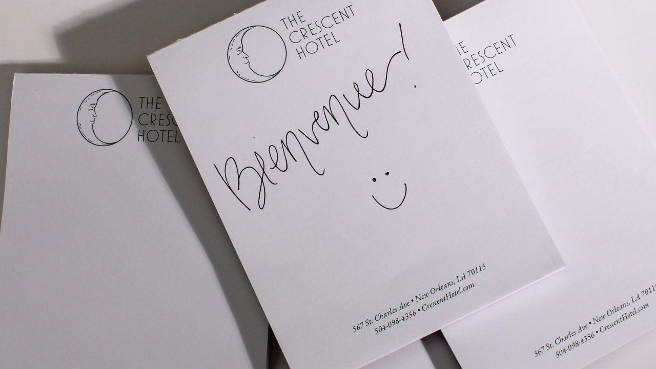 Three sheets of The Crescent Hotel stationery; the top sheet has Bienvenue! and a smiley face handwritten in black ink.