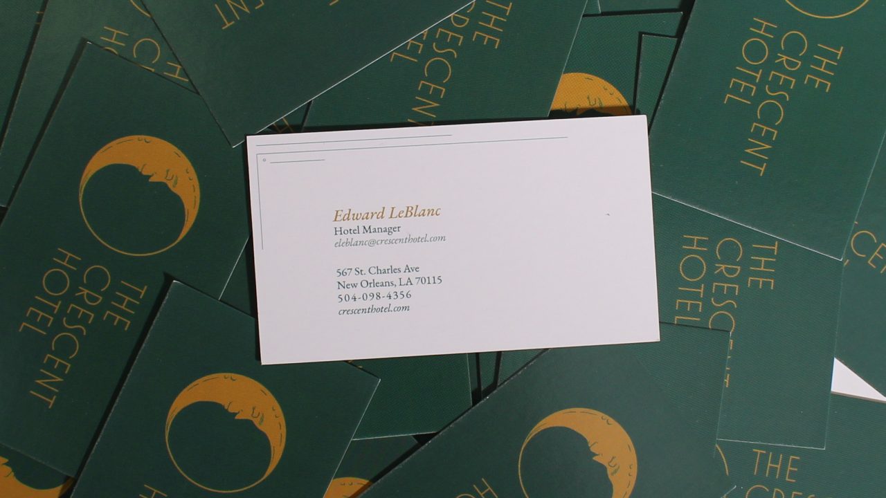 A business card for Eduard LeBlanc, Hotel Manager at The Crescent Hotel, rests on a pile of green cards with the hotel’s name and crescent moon logo.