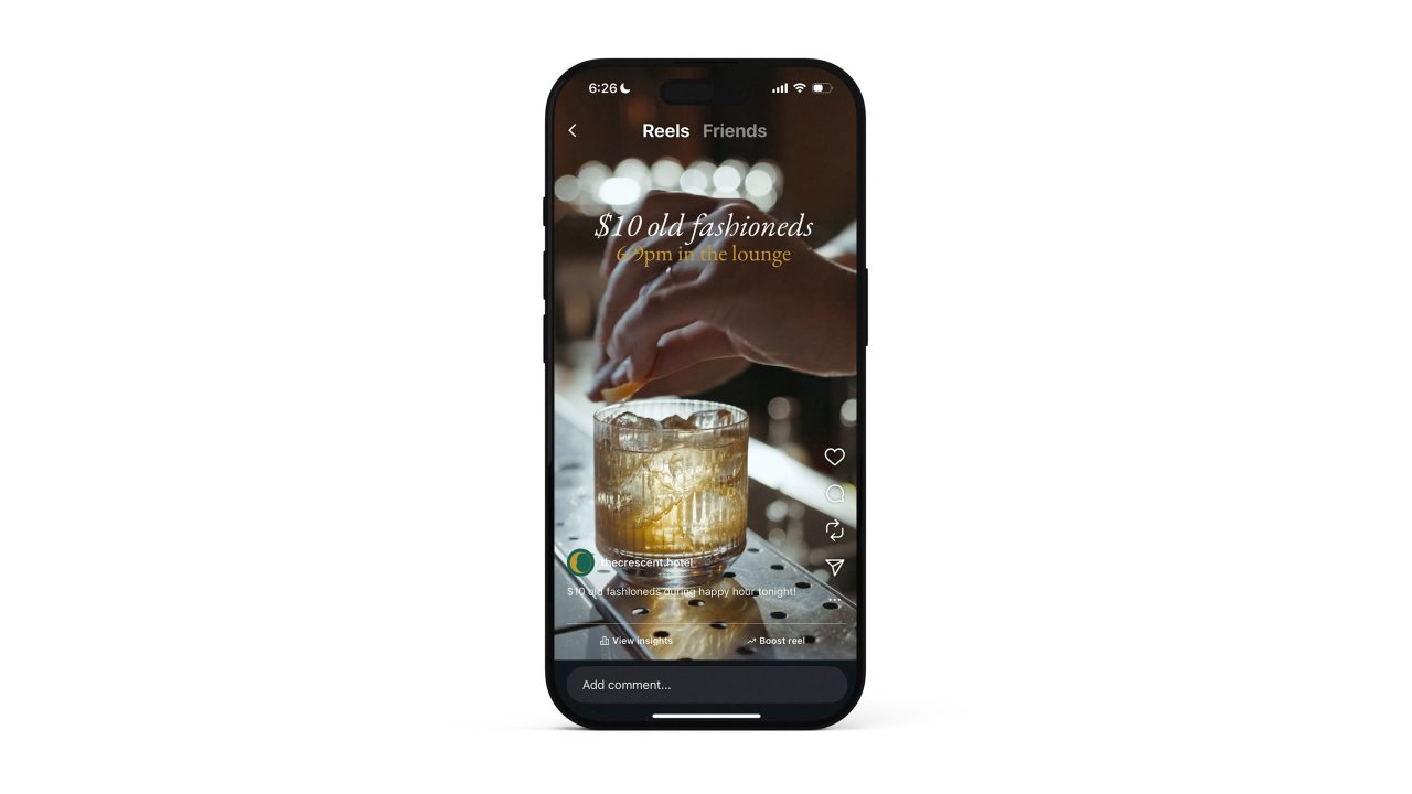 A hand garnishing a glass of cocktail on a bar counter is displayed on a smartphone screen, with text reading $10 old fashioneds 7pm at the lounge.