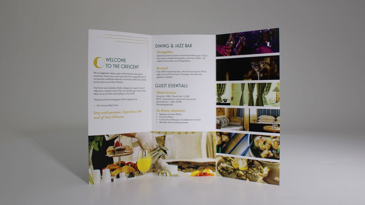 A folded hotel brochure stands open, displaying welcome text, dining and bar information, guest essentials, and photos of food, drinks, and hotel amenities against a plain background.