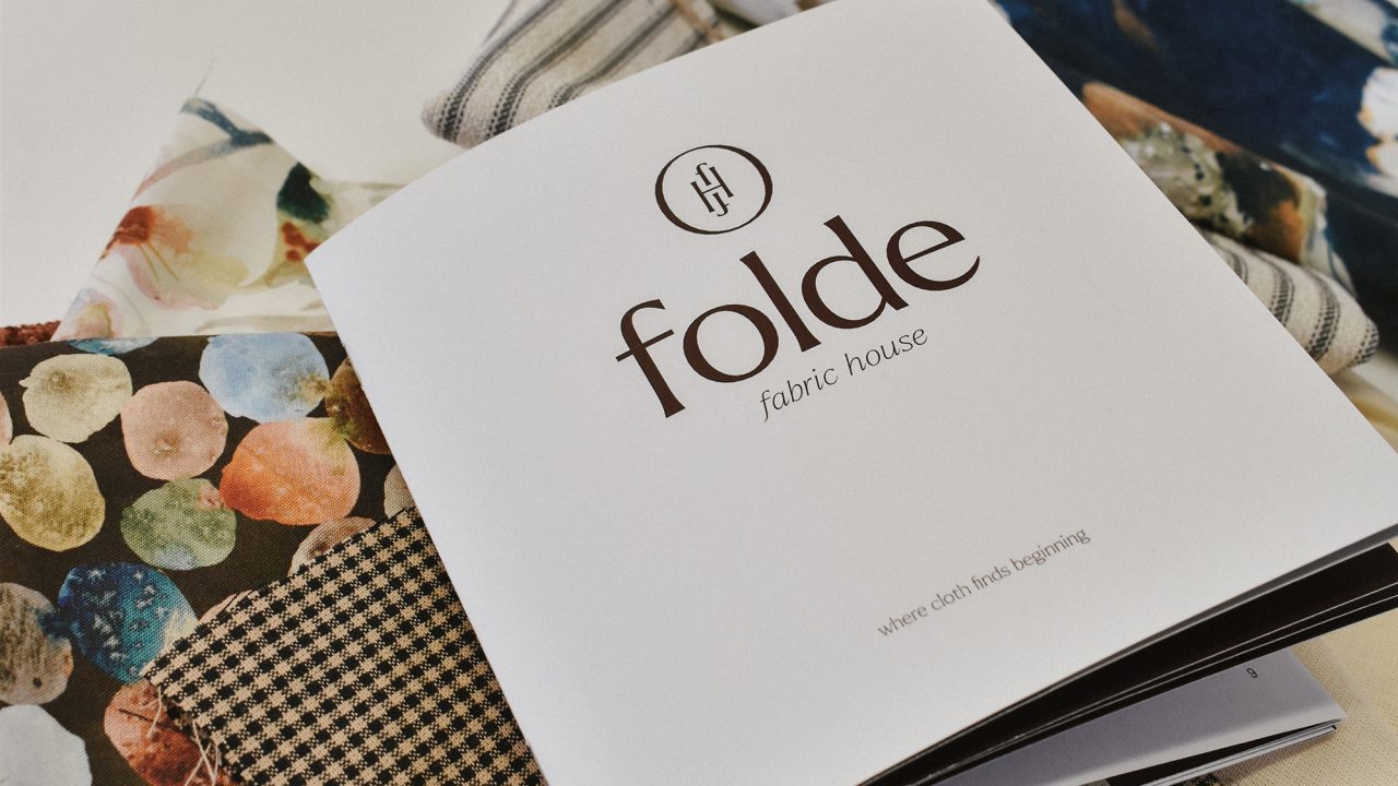 A brochure labeled Folde fabric house rests on top of several patterned fabric swatches, displayed on a white background.