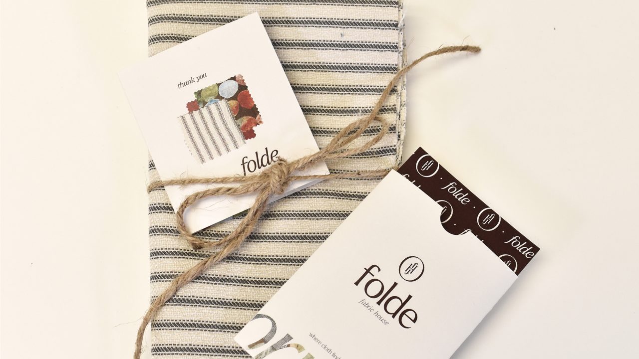 A folded striped cloth with two branded tags and a piece of twine tied around it, displayed on a plain white background.