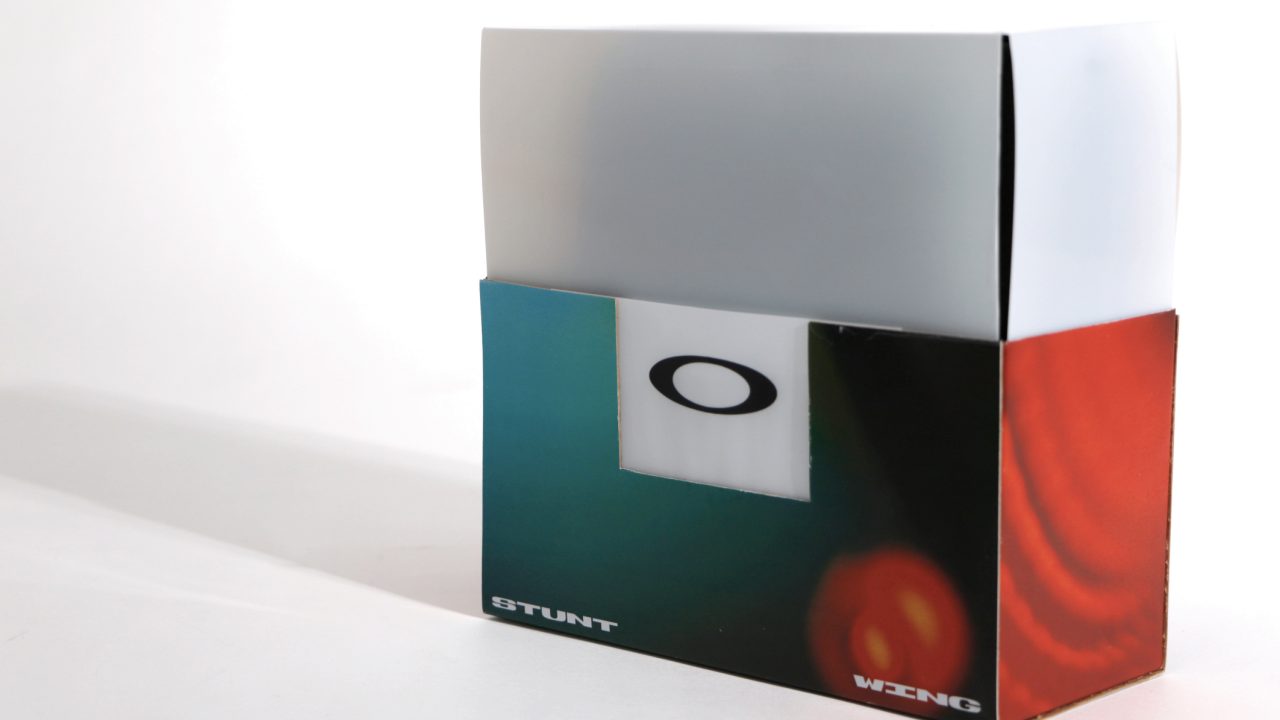 A rectangular box with a white top and colorful lower section featuring the Oakley O logo and the words STUNT and WING on the front.
