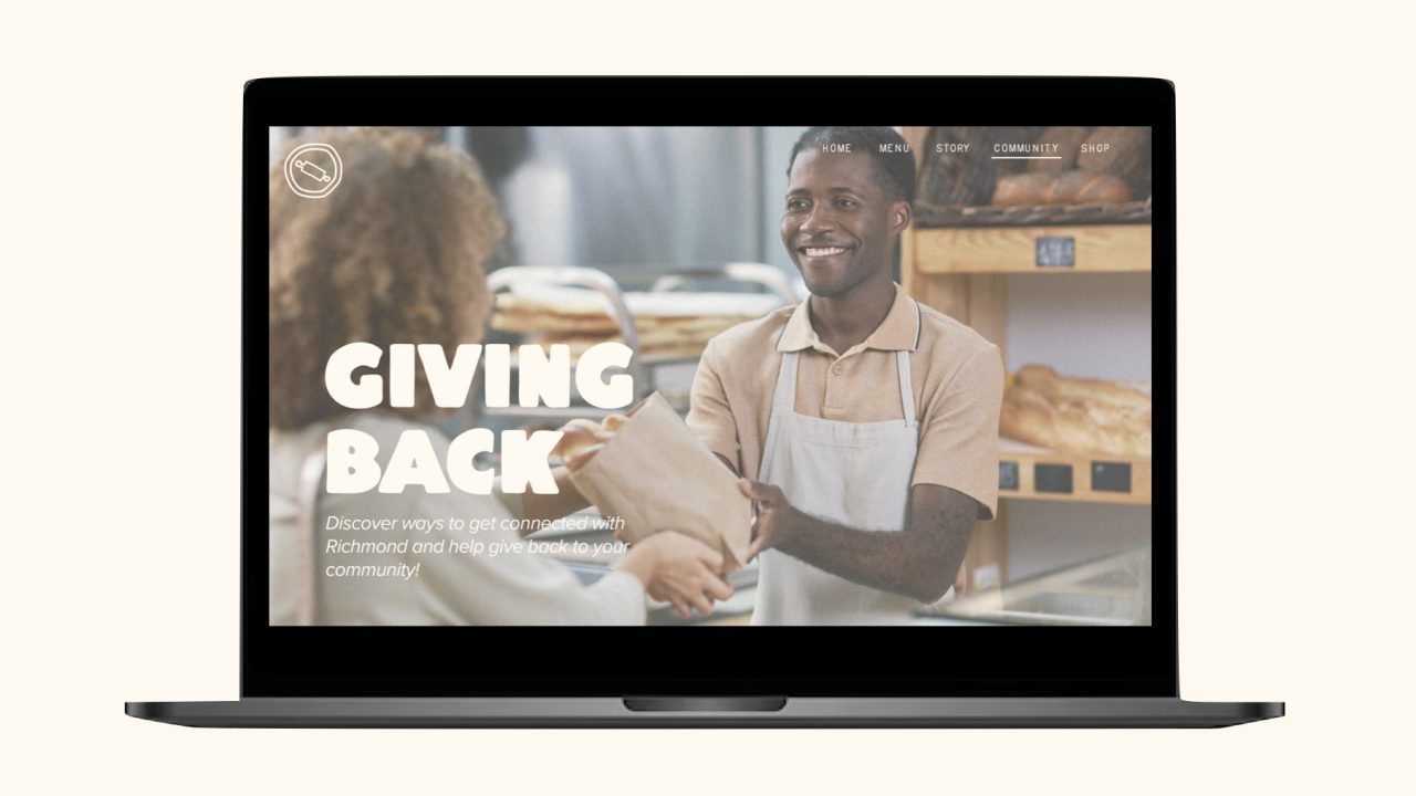 A laptop screen displays a bakery website featuring a smiling employee handing a paper bag to a customer, with bold text reading Giving Back.