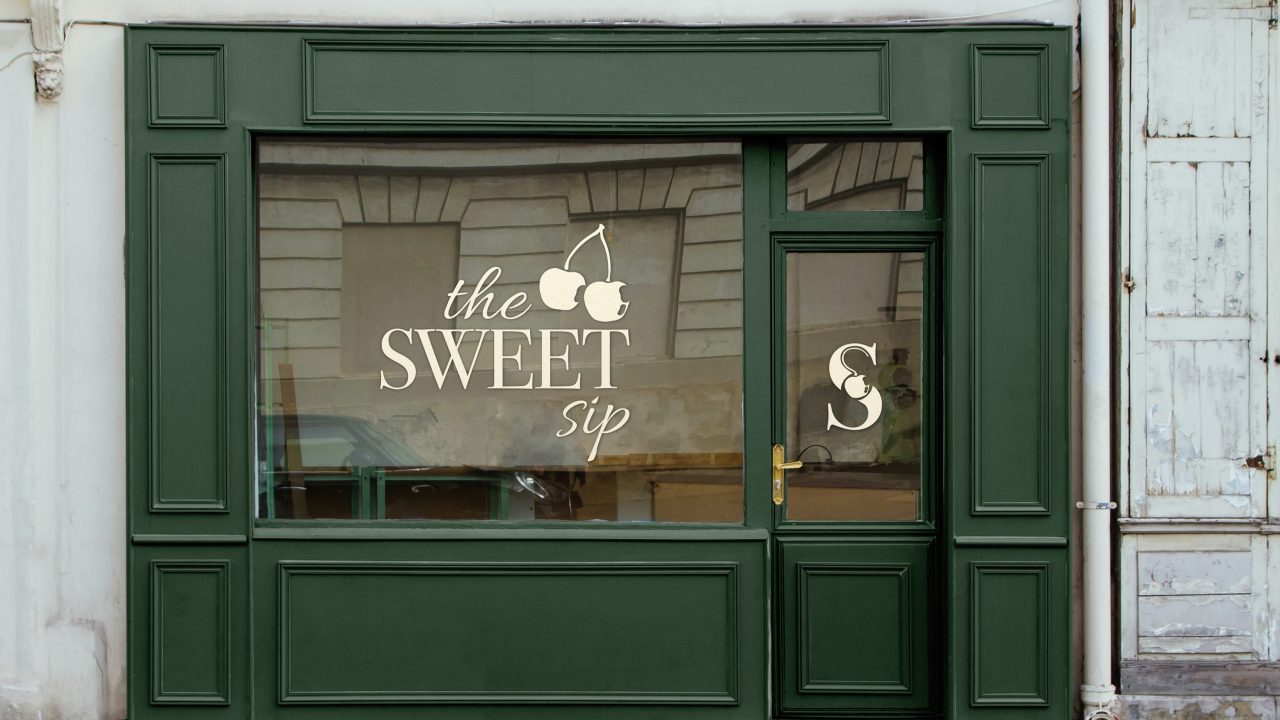 A storefront with dark green panels and a glass window displaying the SWEET sip with cherry graphics; a gold “S” logo is on the door.