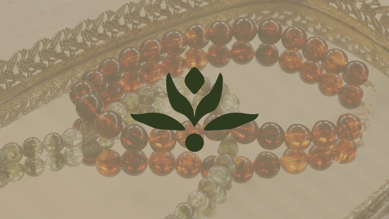 A decorative tray holds beaded necklaces in green and amber tones, overlaid with a green stylized leaf logo in the center.