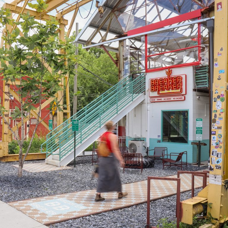 A person walks on a path in front of a building with a Breaker Breaker sign. A yellow industrial crane structure is visible.