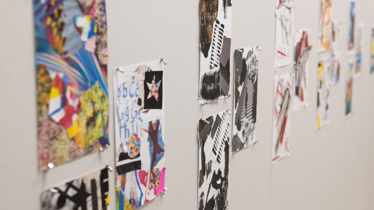 A series of colorful abstract collage artworks are pinned to a white gallery wall in a single horizontal row.