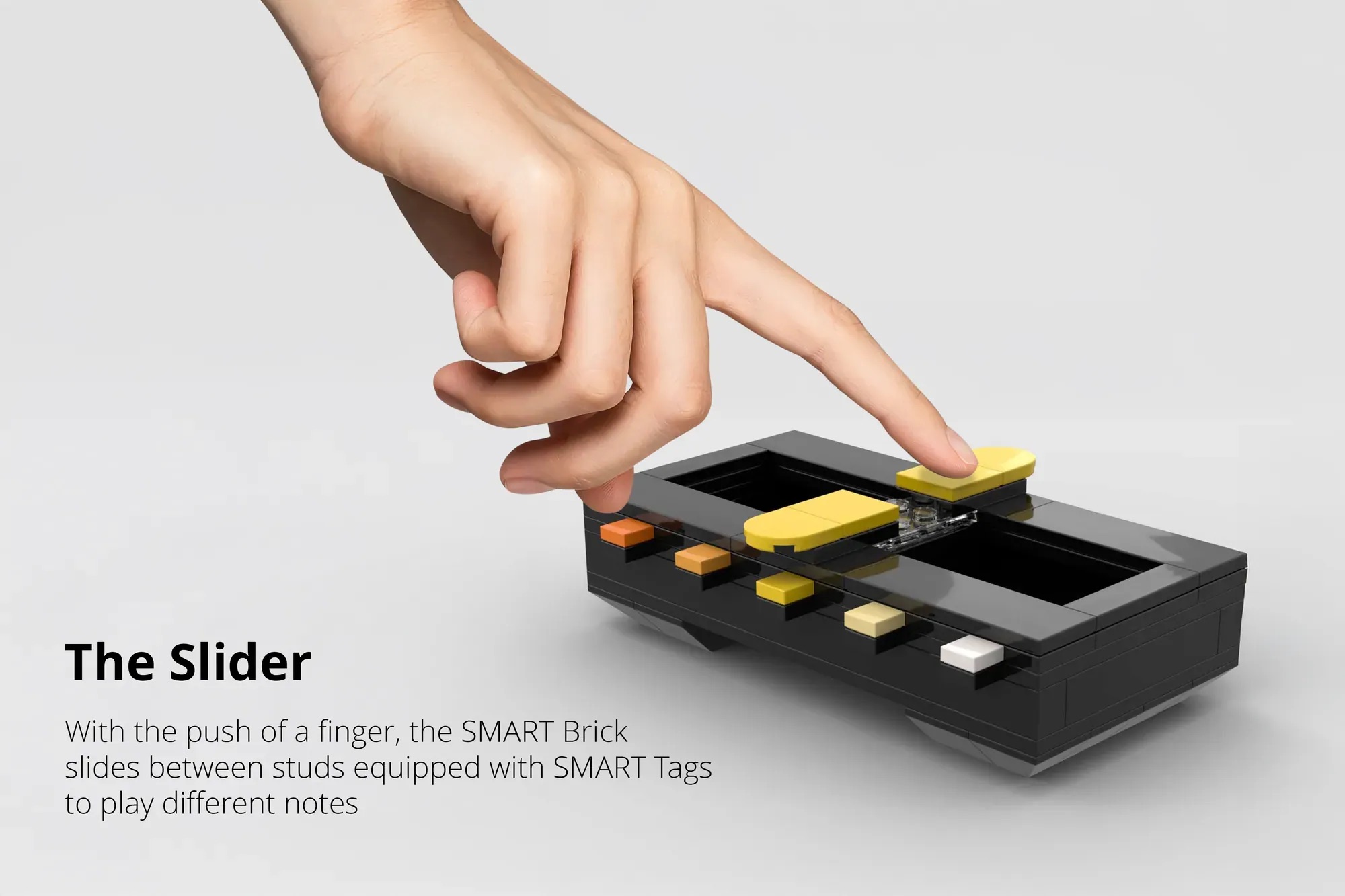 A hand slides a yellow piece on a black LEGO-like device with colored buttons, demonstrating a feature called The Slider for playing different notes.