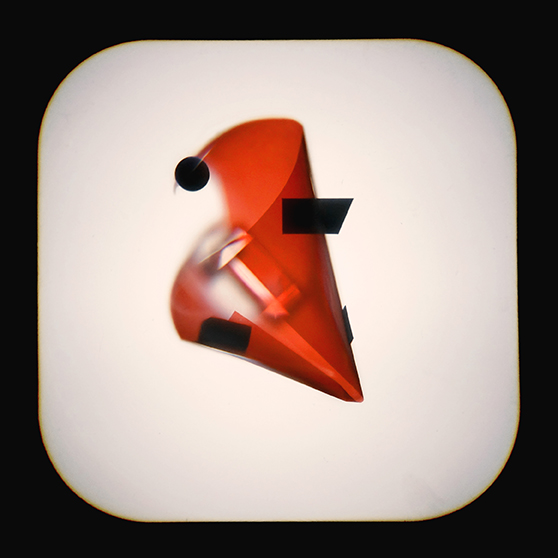 A geometric abstract sculpture with a translucent red cone, black shapes, and a small black sphere, displayed on a softly lit white background.