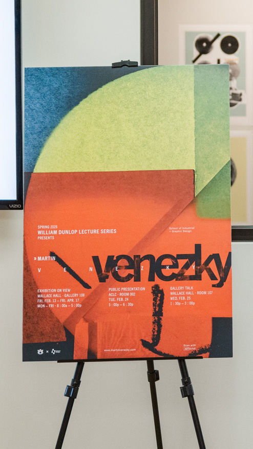 A poster on an easel displays information about the Martin Venezky lecture series at William Dunlop Gallery Hall, featuring dates, times, and event details in bold, modern typography.
