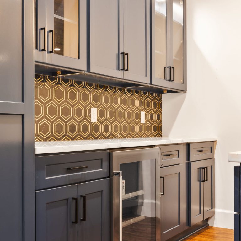 Modern kitchen with dark gray cabinets, patterned hexagon tile backsplash, white countertops, a mini fridge, and wood flooring.