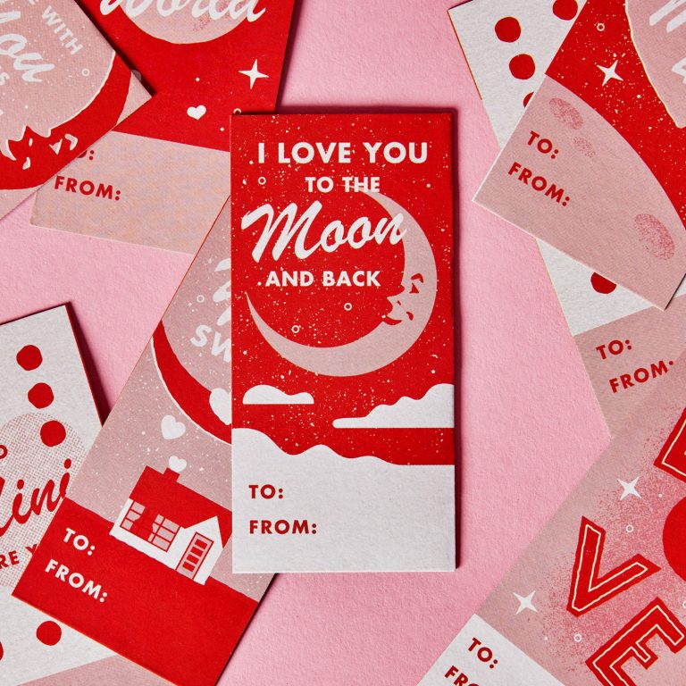 Assorted red and pink Valentines Day cards with romantic messages, including I love you to the moon and back, arranged on a pink surface.