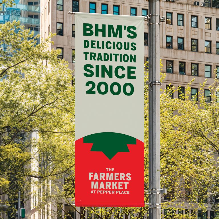Vertical sign on a city street reads BHMs Delicious Tradition Since 2000. The Farmers Market at Pepper Place with a tomato graphic. Trees and buildings are visible in the background.