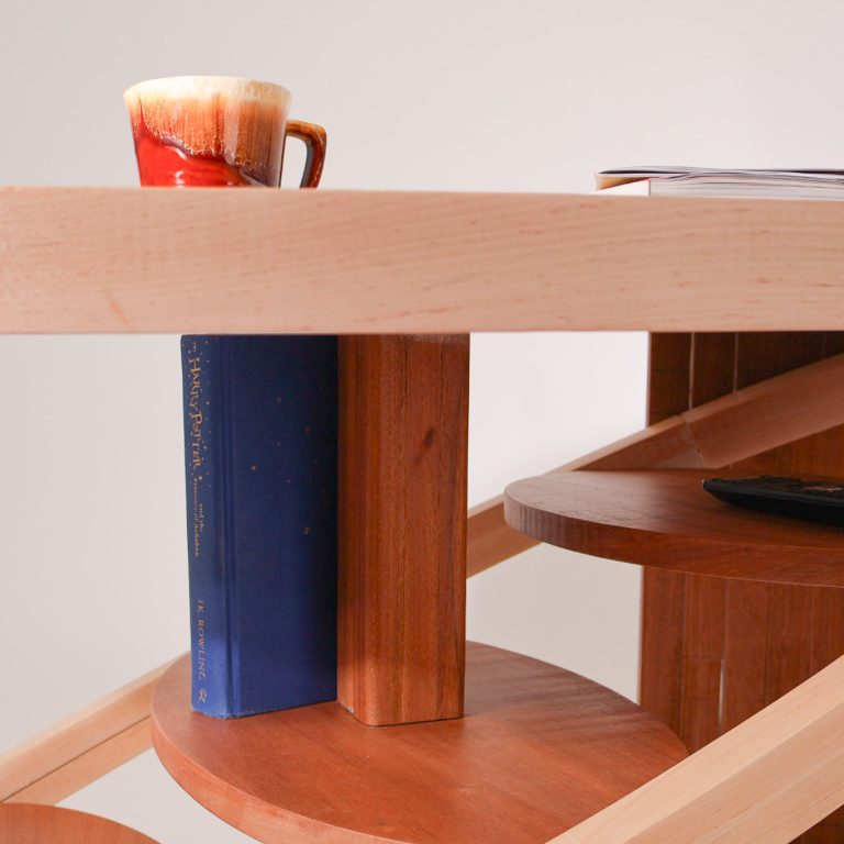 A wooden desk with curved supports, holding a mug, a blue book, two notebooks, and a black remote control.