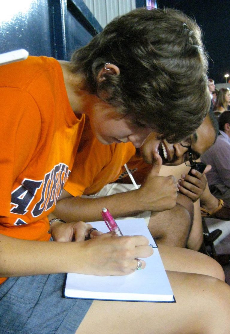 A person in an orange Auburn shirt signs an autograph for a fan.